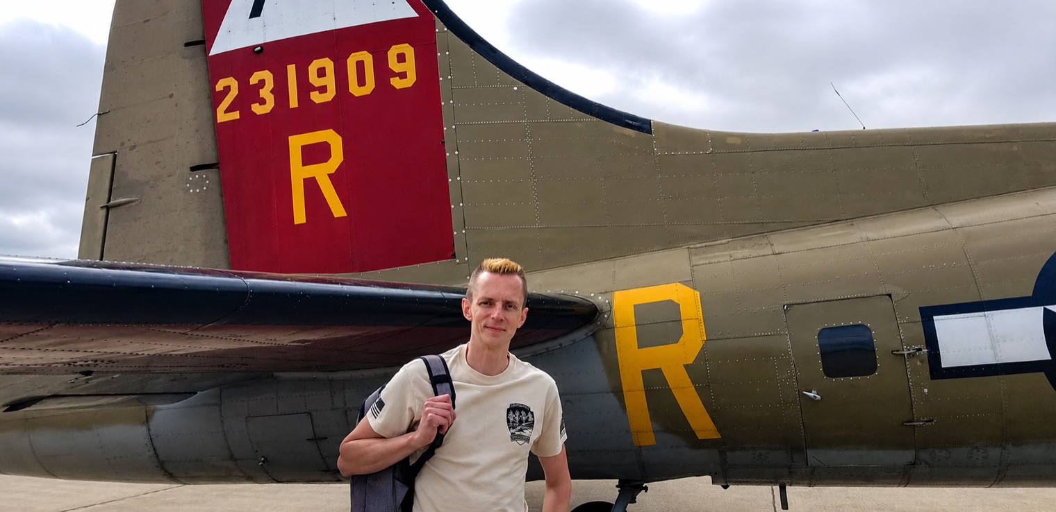 Aleh Haiko in front of a B-17 bomber, a backpack over one shoulder.